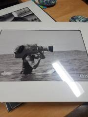 Production Still, Big Wednesday: photograph of George Greenough in the water on a surf mat, face obscured by a film camera.